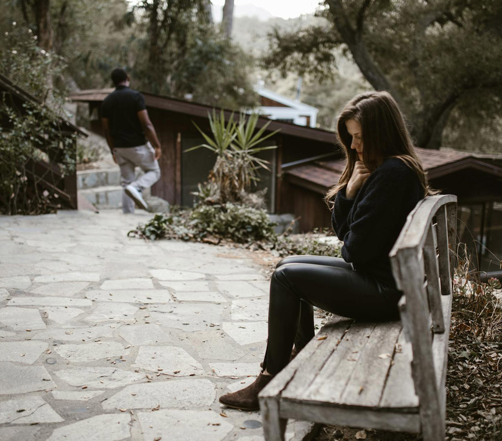 Thoughtful woman sitting on a bench with man working away after divorce