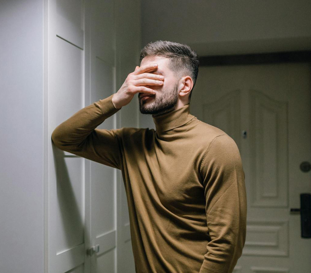 Depressed man leaning against the wall and covering his face